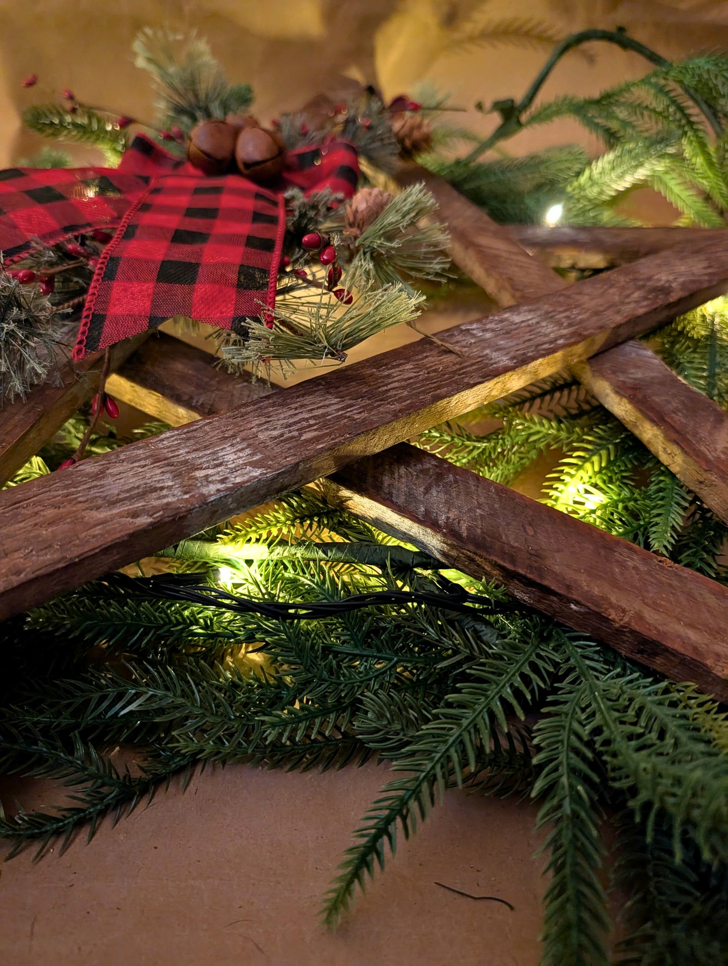 Decorative arrangement with greenery, wooden planks, and a red and black checkered ribbon.