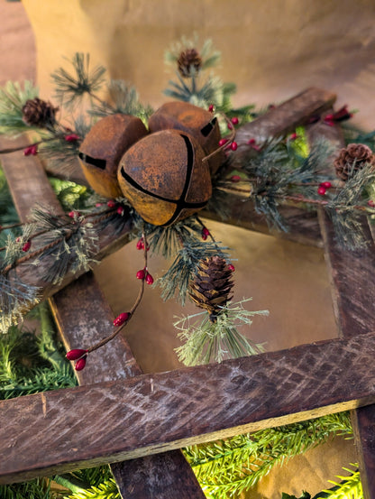 Decorative wreath with rusty bells, pine cones, and greenery on a wooden surface.