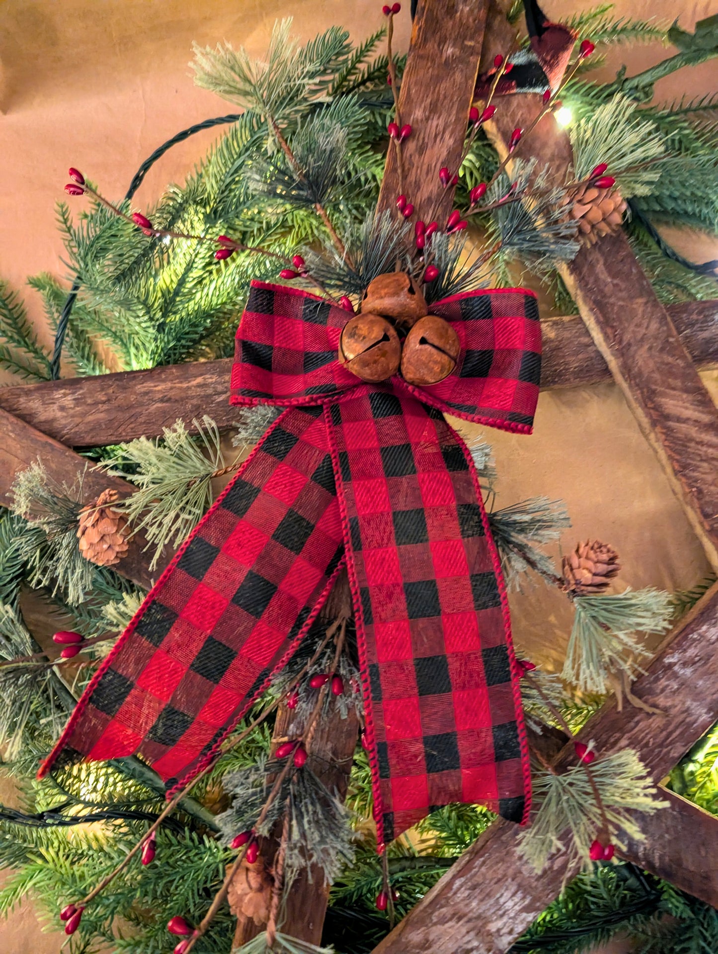 Decorative Christmas bow with red and black plaid pattern on a green wreath with pine cones and berries.