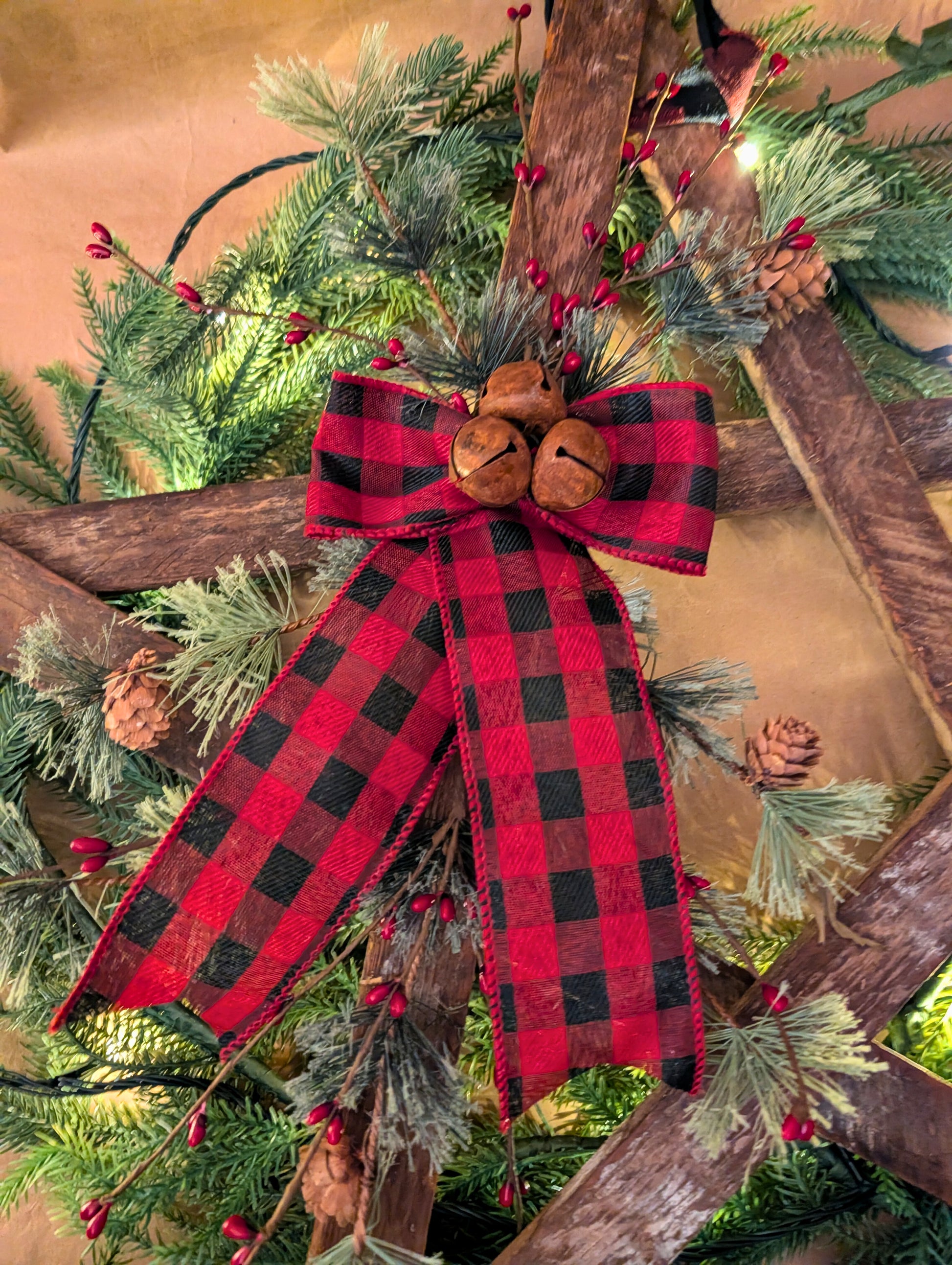 Decorative Christmas bow with red and black plaid pattern on a green wreath with pine cones and berries.