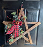Wooden star decoration with greenery and a red plaid bow on a black door.