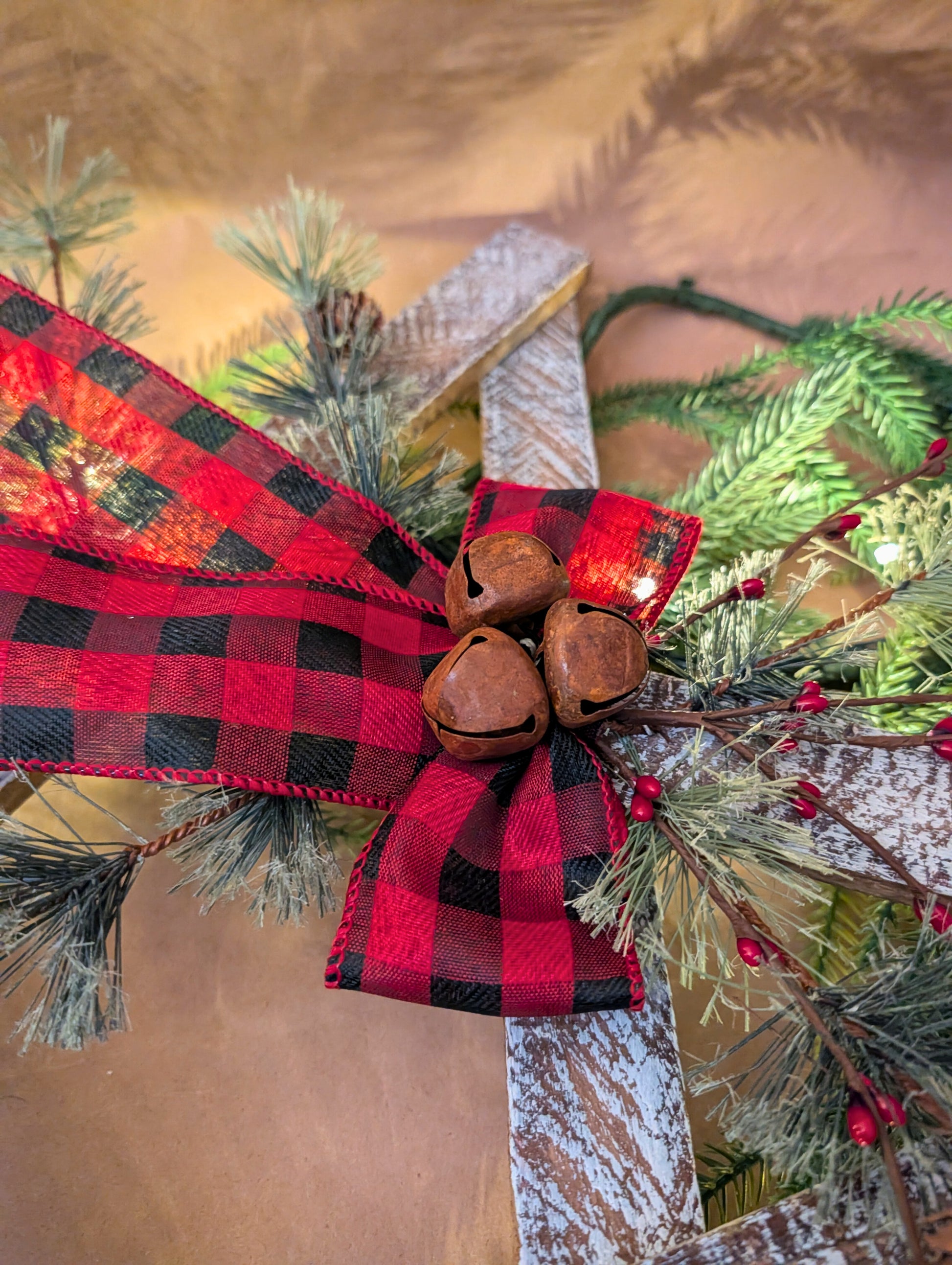Decorative Christmas swag with red and black plaid ribbon and wooden bells on a blurred natural background.
