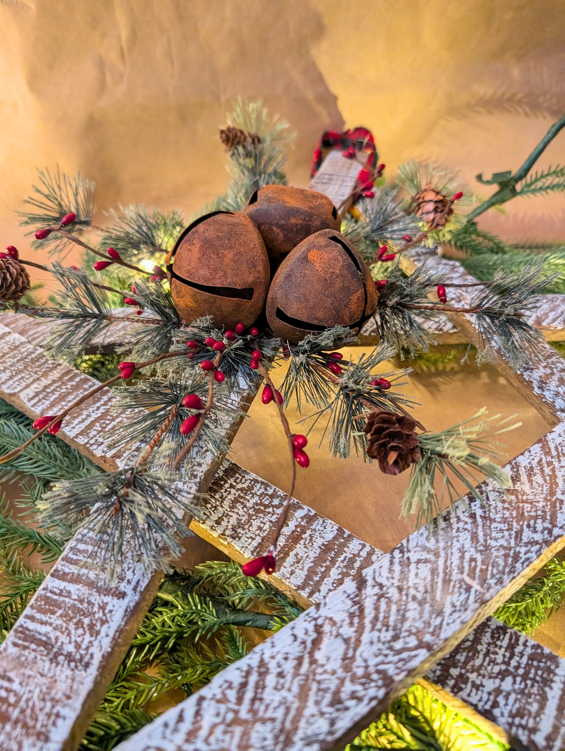 Decorative wreath with rusty bells, pine cones, and red berries on a wooden background.