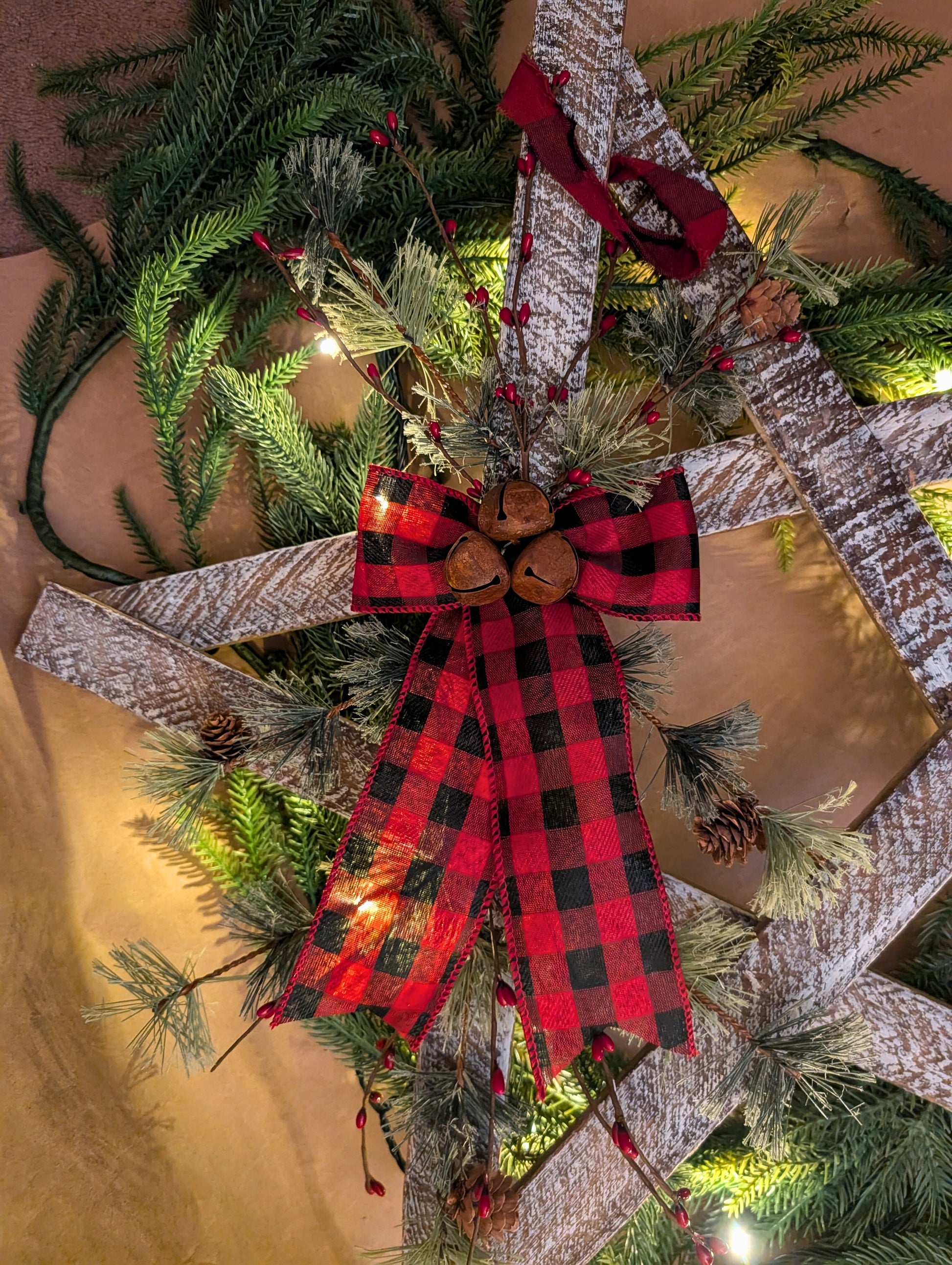 Decorative wreath with red plaid bow, pine cones, and lights on a neutral background