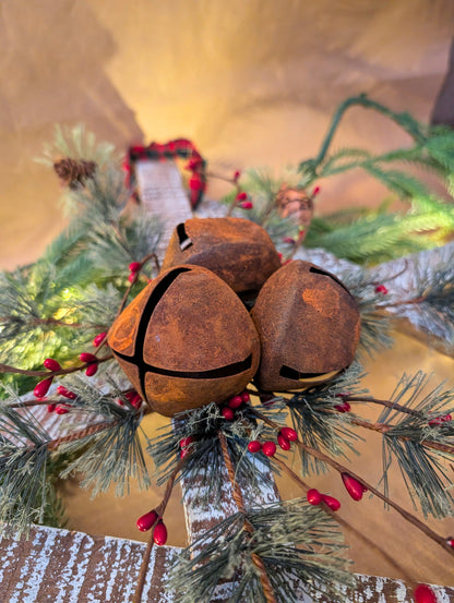 Rust-colored jingle bells on a Christmas wreath with greenery and red berries.