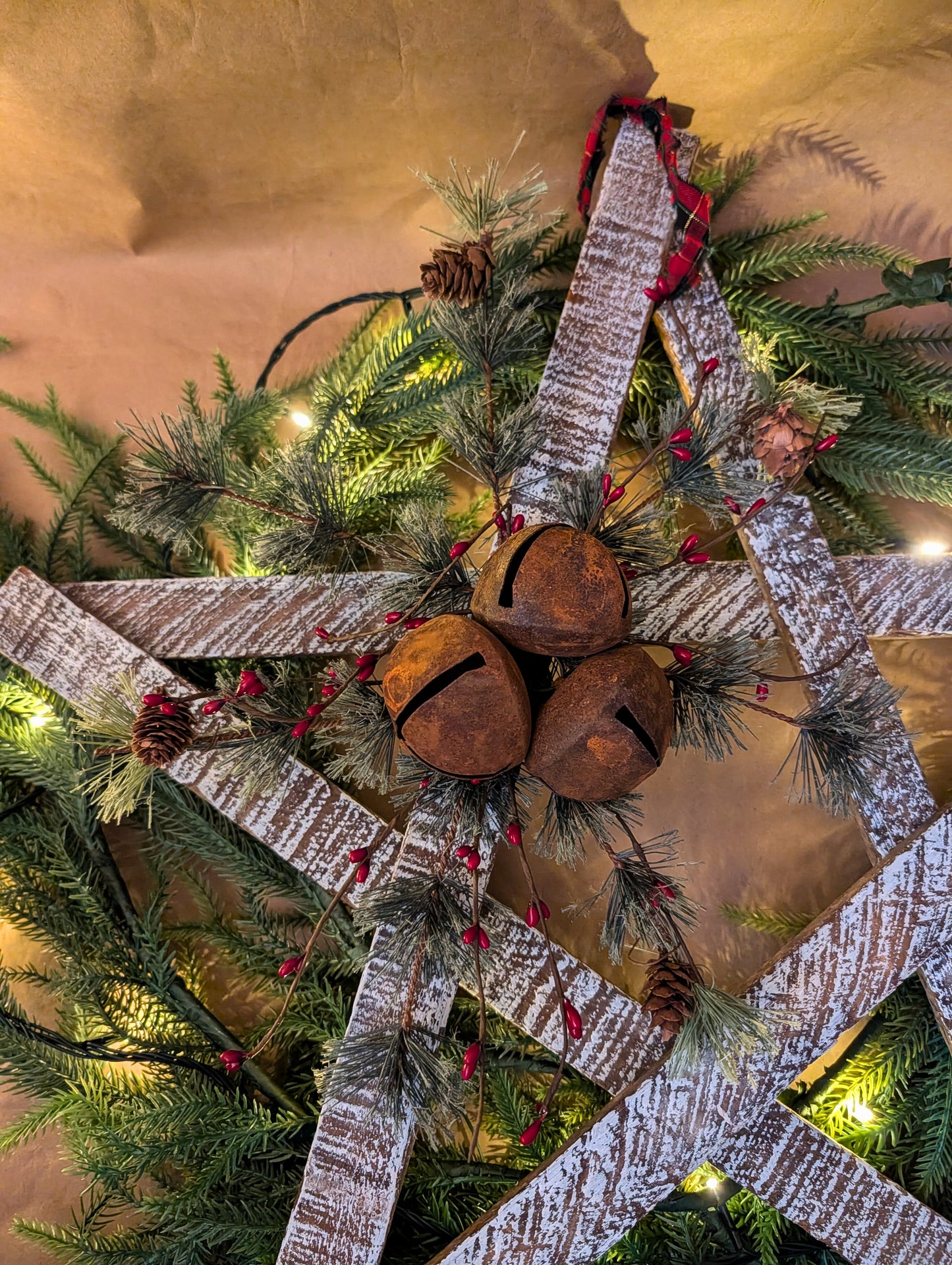 Decorative wreath with rusted bells and plaid ribbon on a wooden door.