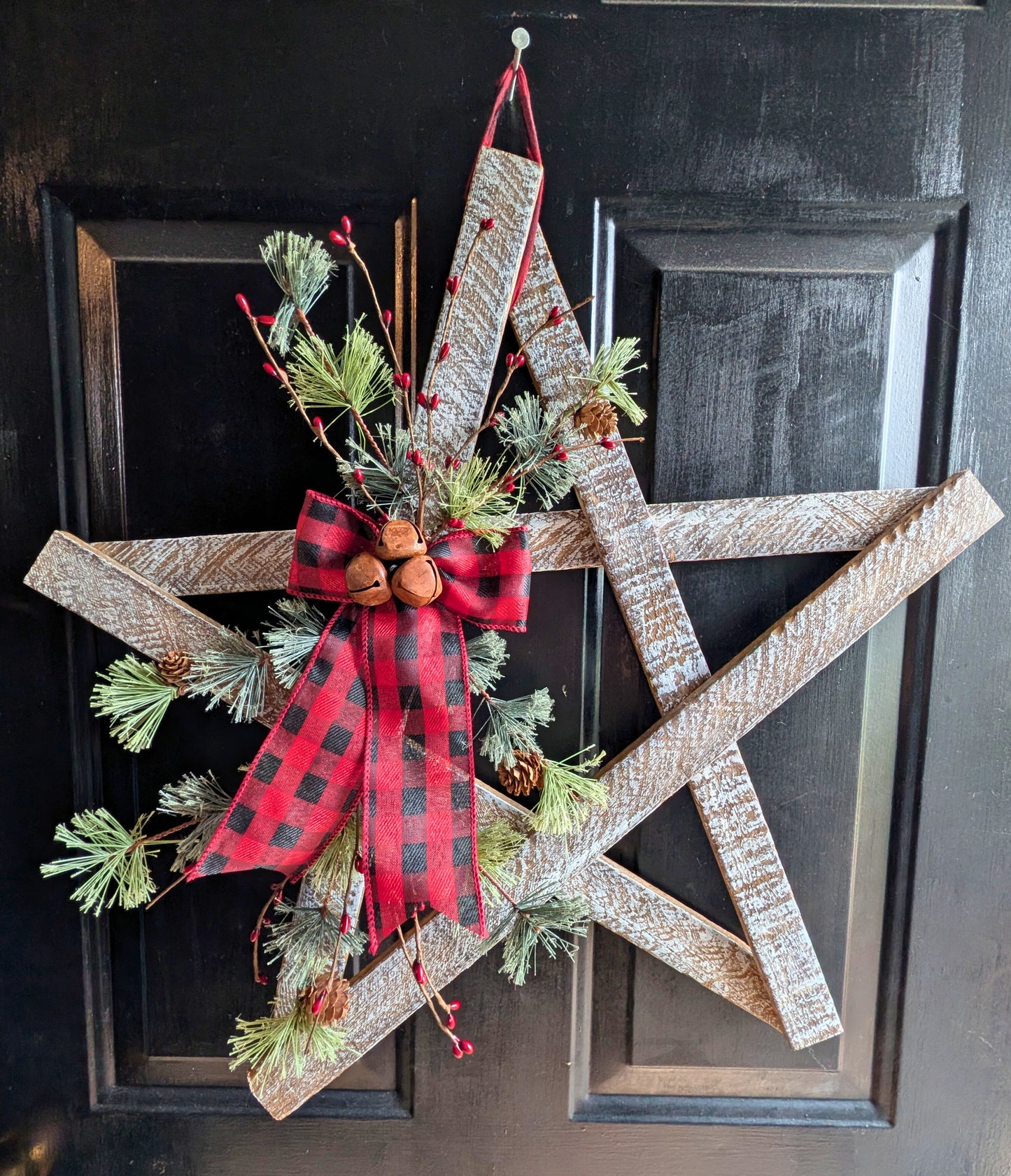 Decorative Christmas wreath with a red plaid bow on a black door.