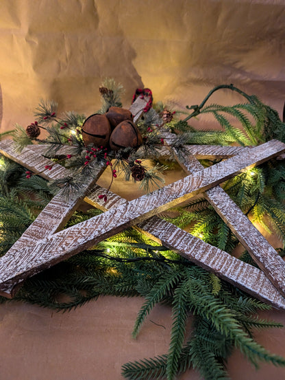 Decorative wreath with greenery, wooden elements, and pinecones on a neutral background