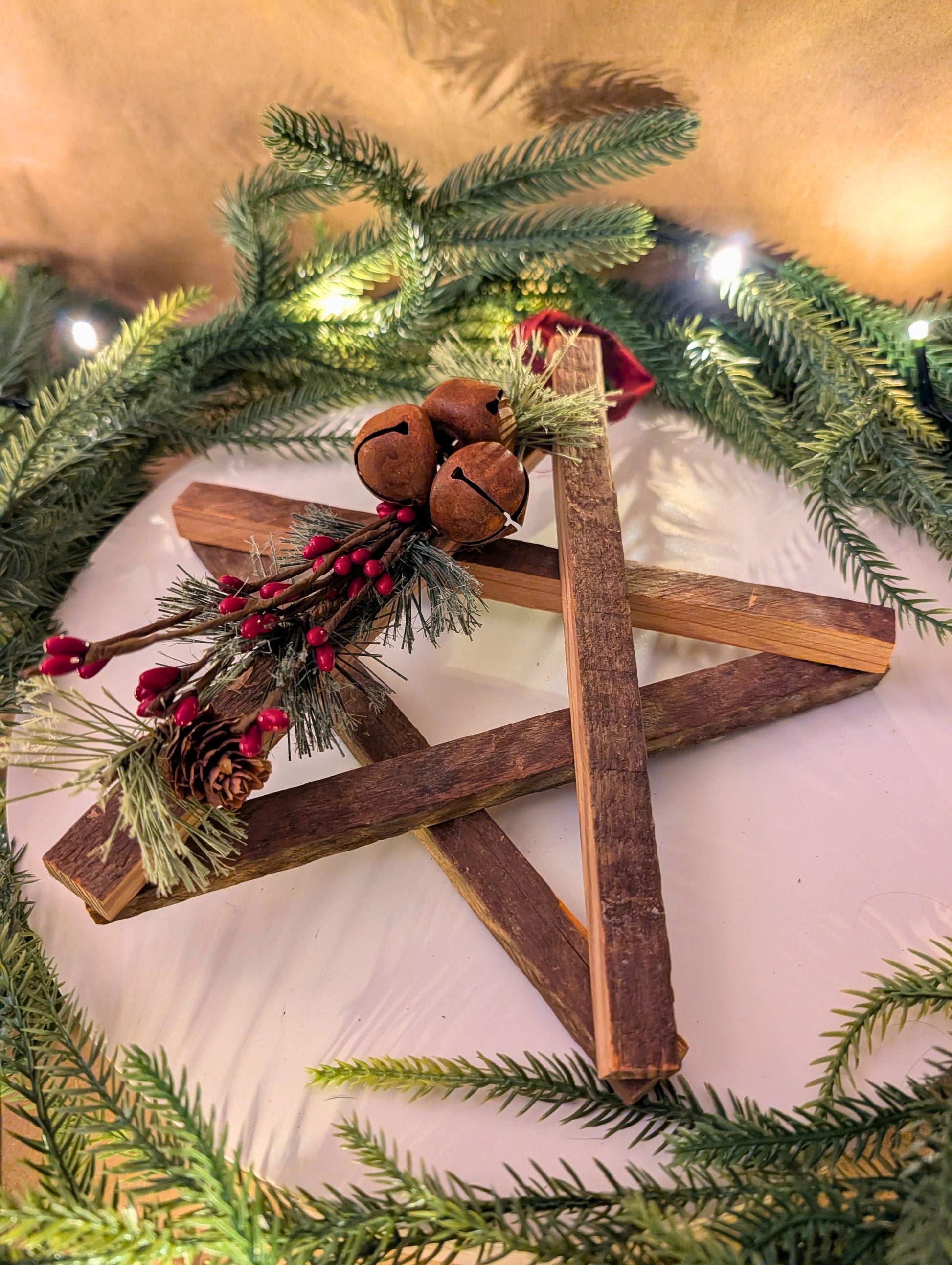 Wooden star ornament with pine branches and jingle bells on a Christmas tree.
