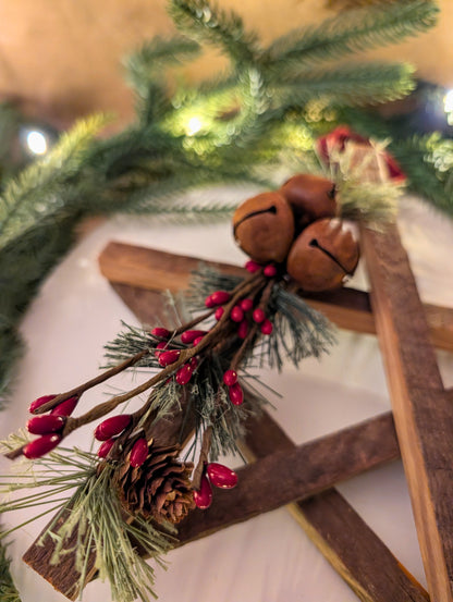 Decorative arrangement with pine branches, red berries, and pinecones on a wooden cross.