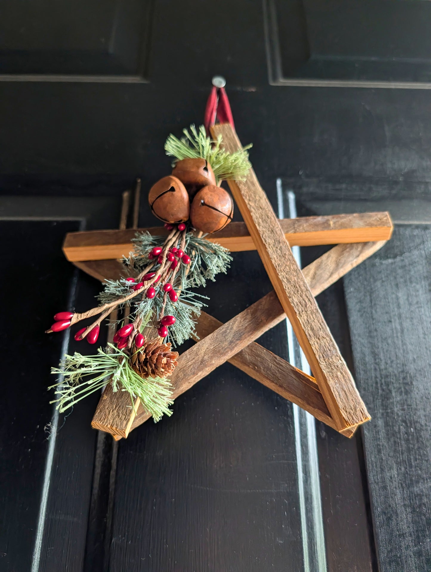 Wooden star decoration with jingle bells and greenery on a black surface