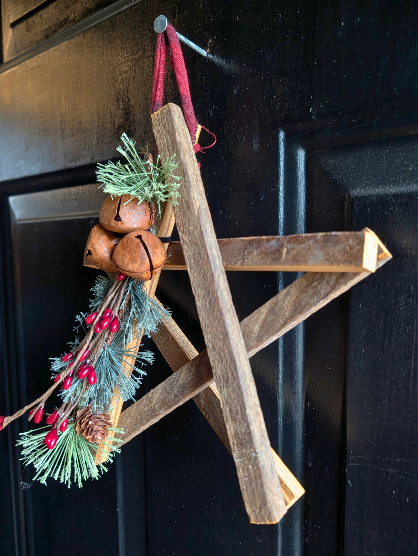Wooden star ornament with pine branches and bells on a dark background