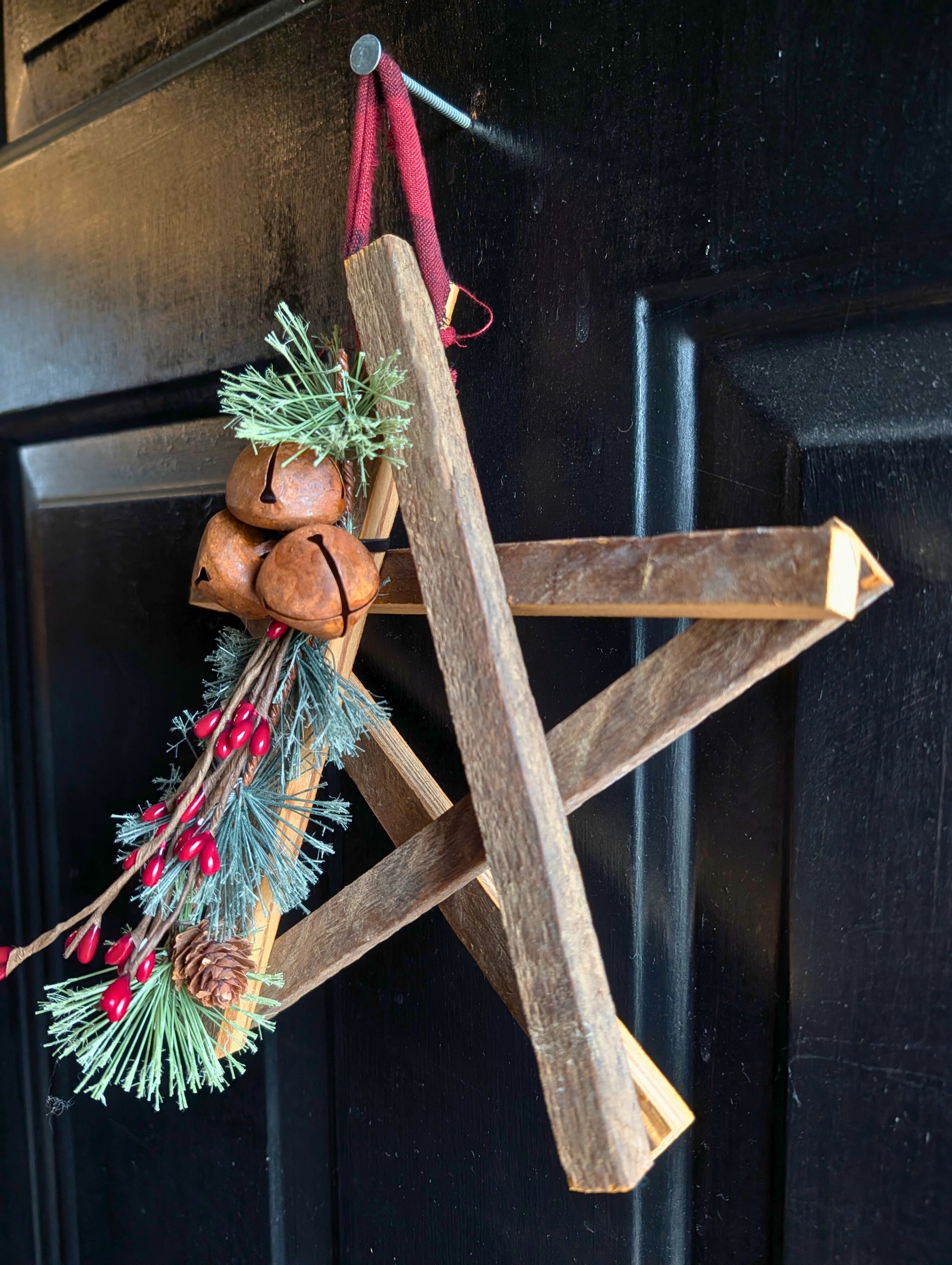 Wooden star ornament with pine branches and bells on a dark background