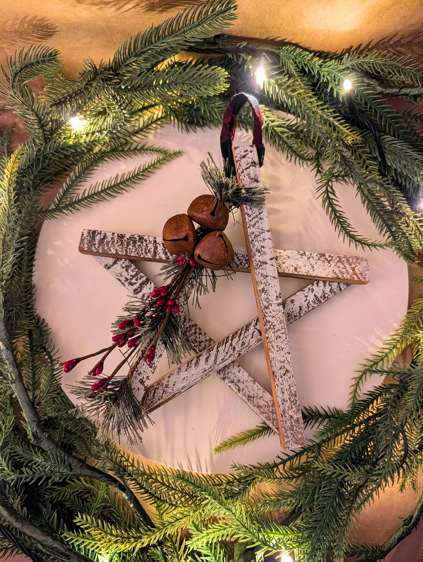 Decorative wreath with star-shaped wooden ornament, jingle bells, and greenery on a white background.