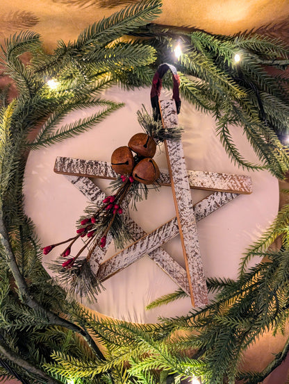 Decorative wreath with star-shaped wooden ornament, jingle bells, and greenery on a white background.