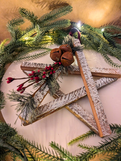 Decorative star with greenery, jingle bells, and red berries on a light background