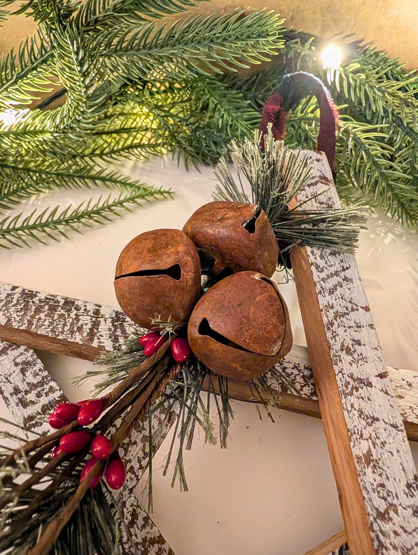 Decorative arrangement with rusted bells, greenery, and red berries on a wooden surface.