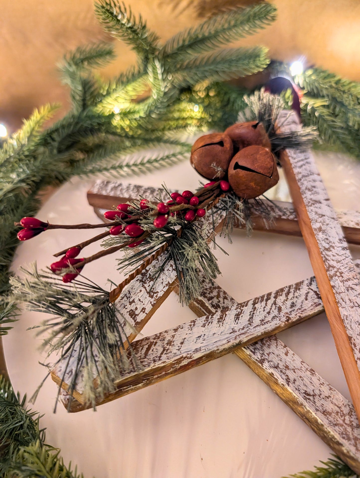 Decorative star with greenery, red berries, and wooden jingles on a white surface.